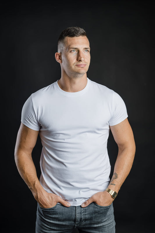 Moški nosi belo majico FIT znamke Slovenski Patriot in gleda vstran. Fotografija prikazuje udoben kroj, prileganje in kakovostno izdelavo majice.