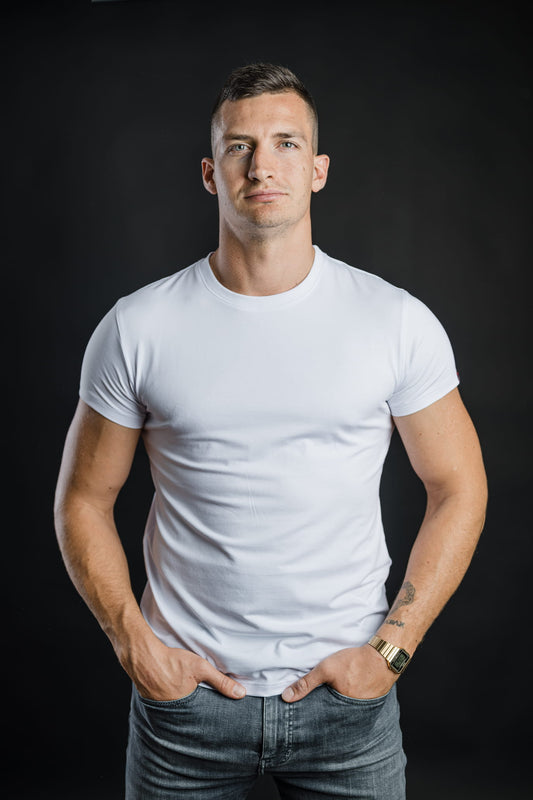 Moški nosi belo majico FIT znamke Slovenski Patriot. Klasičen kroj, udobno prileganje in minimalističen dizajn iz kakovostnega bombaža, narejeno v Sloveniji.