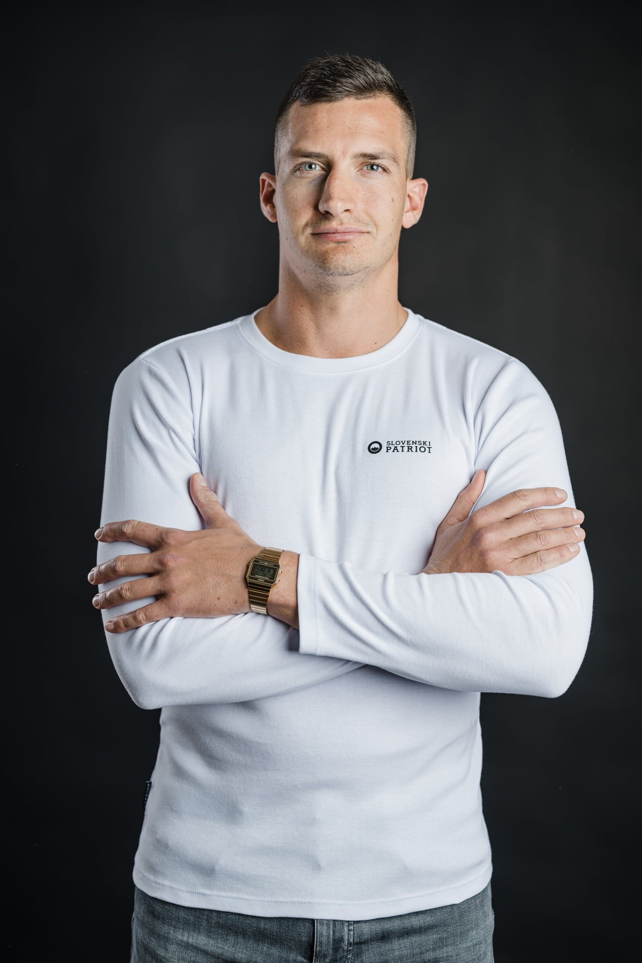 Moški s prekrižanimi rokami nosi belo 100% bombažno majico z dolgimi rokavi Tech Pro znamke Slovenski Patriot, narejeno v Sloveniji.