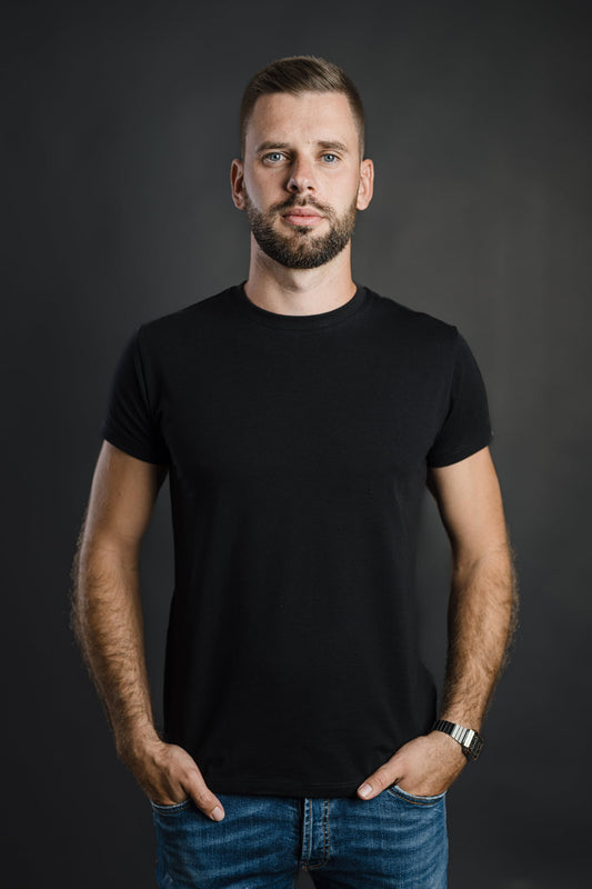 Moški nosi črno majico FIT znamke Slovenski Patriot, narejeno v Sloveniji iz kakovostnega bombaža, s preprostim in oprijetim krojem, idealna za vsakdanjo uporabo.