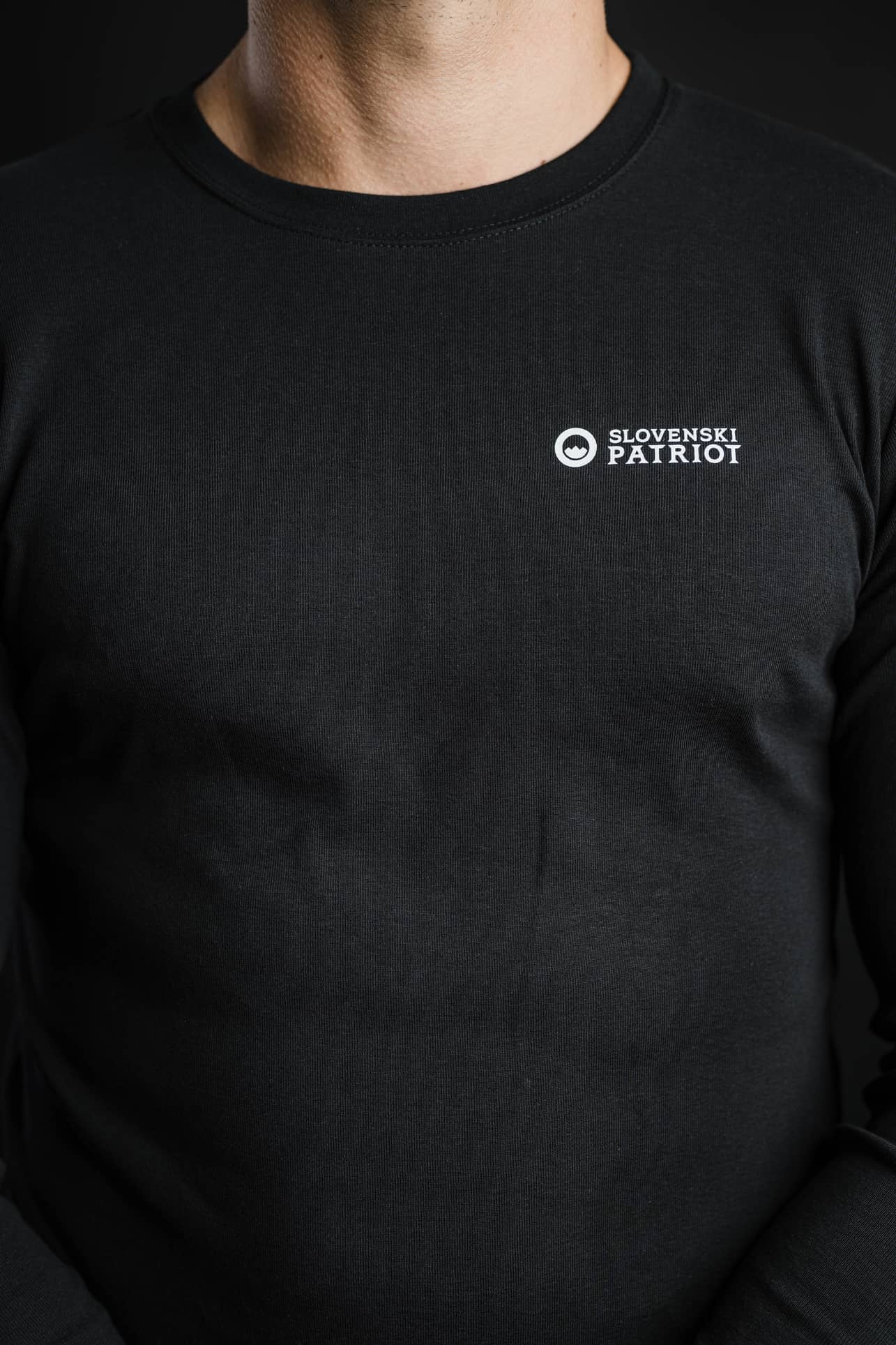 Detajl črne 100% bombažne majice z dolgimi rokavi Tech Pro znamke Slovenski Patriot, z belim logotipom na prsnem delu, narejeno v Sloveniji.