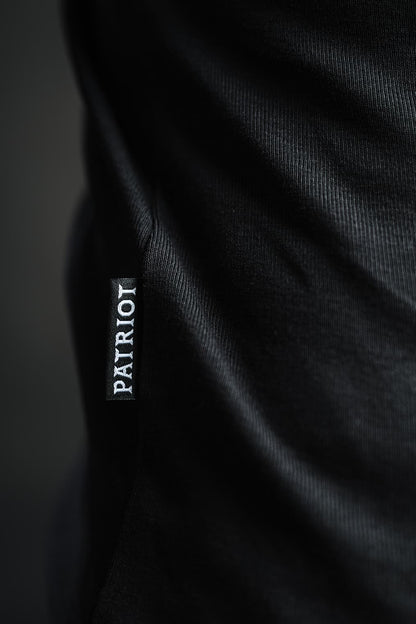 Detajl črne etikete z napisom PATRIOT, všite v stranski rob črne majice z dolgimi rokavi TECH PRO, narejene v Sloveniji.