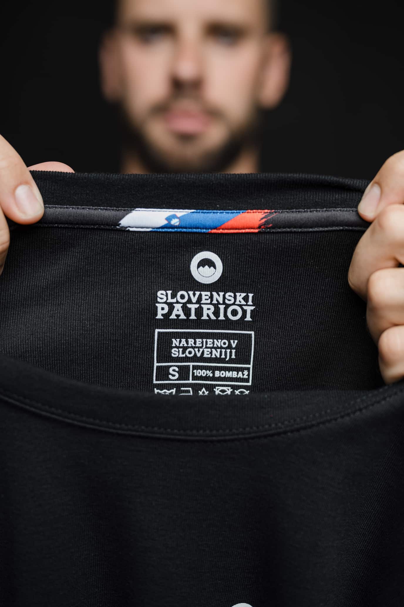 Detajl notranje etikete črne majice Tech Pro znamke Slovenski Patriot z napisom Narejeno v Sloveniji in oznako 100% bomba ter slovensko zastavo.