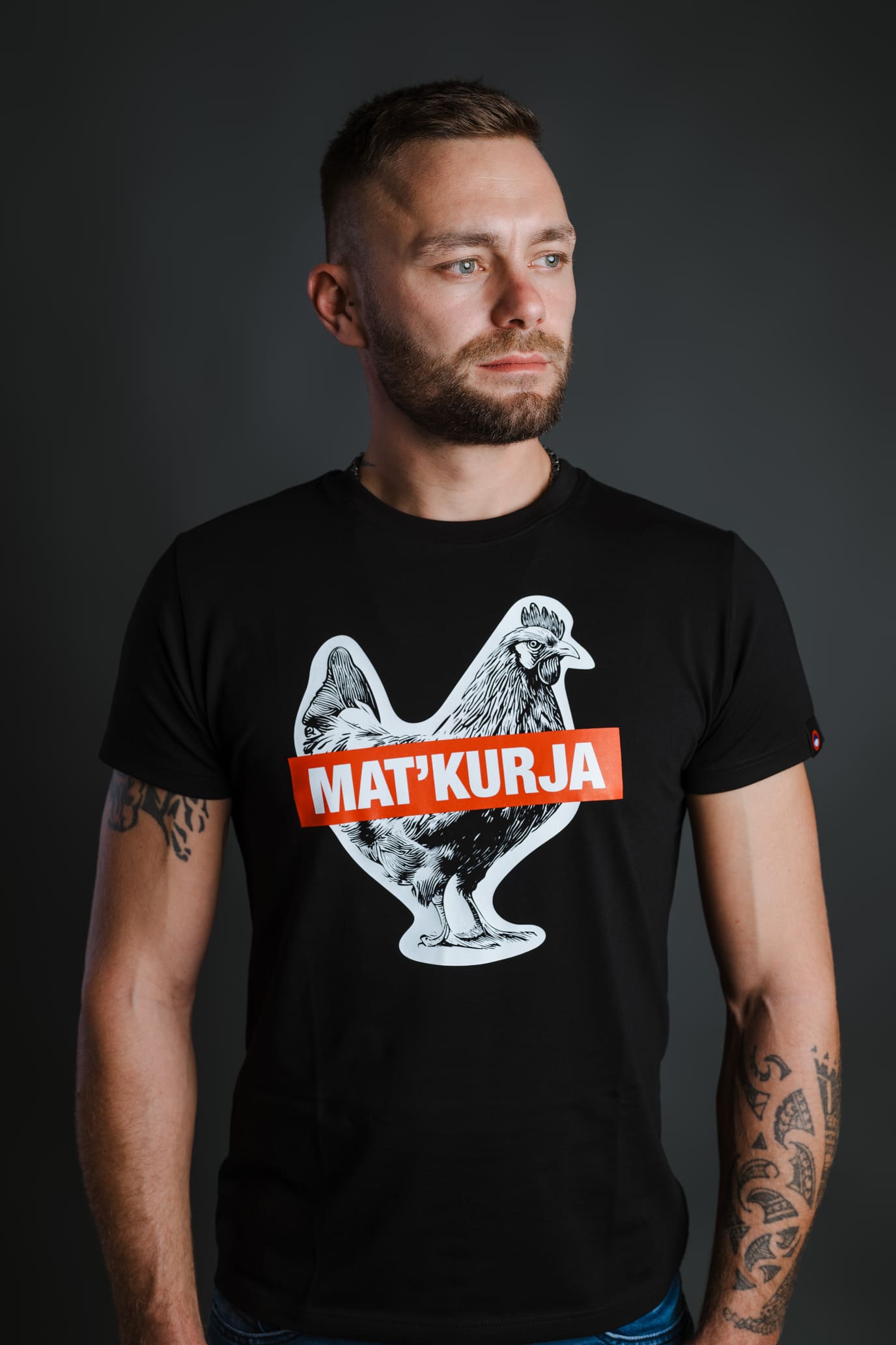 Moški nosi črno bombažno majico Matkurja znamke Slovenski Patriot, narejeno v Sloveniji, prikazano iz portretnega kota.