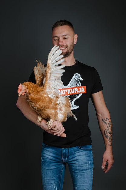 Moški v jeans hlačah drži kokoš in nosi črno bombažno majico Matkurja znamke Slovenski Patriot, narejeno v Sloveniji.