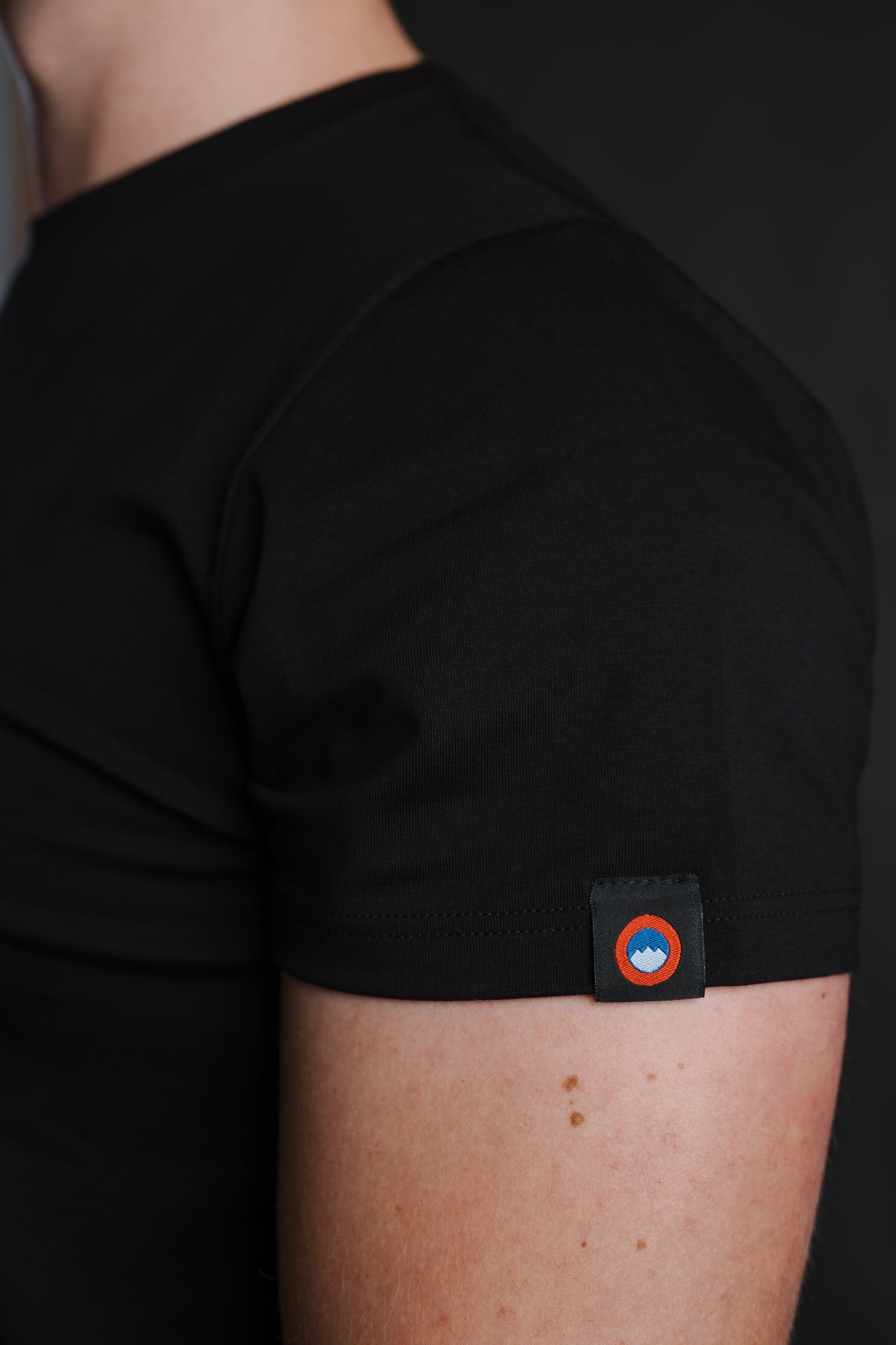 Detajl črne bombažne majice Slovenski Patriot z našitim logotipom na rokavu, narejeno v Sloveniji.