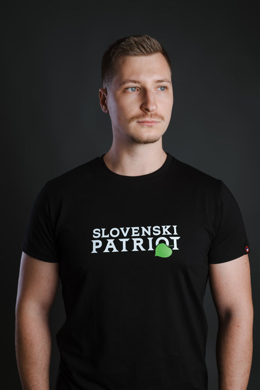 Moški nosi črno bombažno majico Slovenski Patriot z zelenim lipovim listom, prikazano iz portretnega kota, narejeno v Sloveniji.
