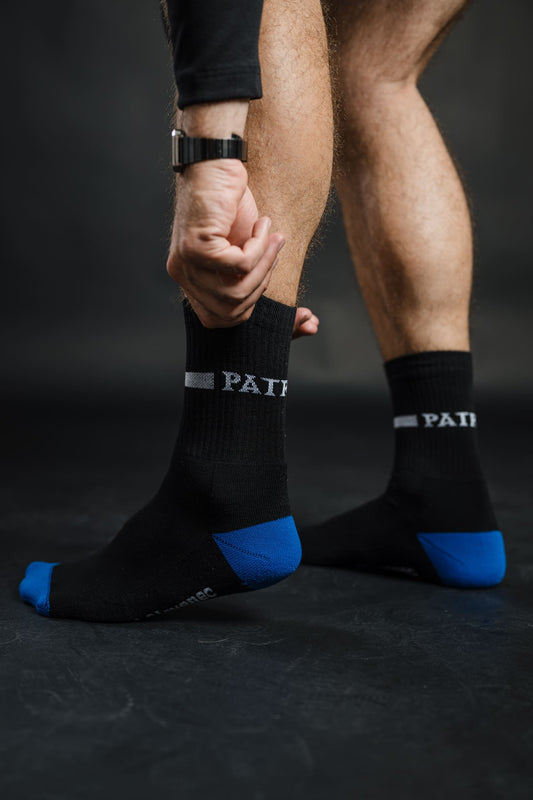 Črne nogavice Patriot z modrimi petami in prsti ter napisom “PATRIOT” v beli barvi. Športno-elegantne nogavice, zasnovane za udobje in trajnost.