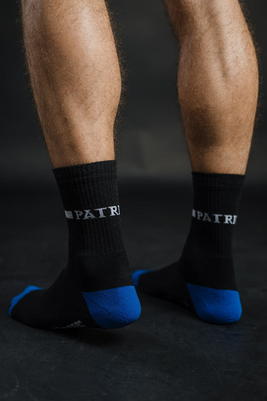 Zadnji pogled na črne nogavice Patriot z modrimi petami in napisom “PATRIOT”. Kakovostne in udobne nogavice, primerne za vsakdan in šport.