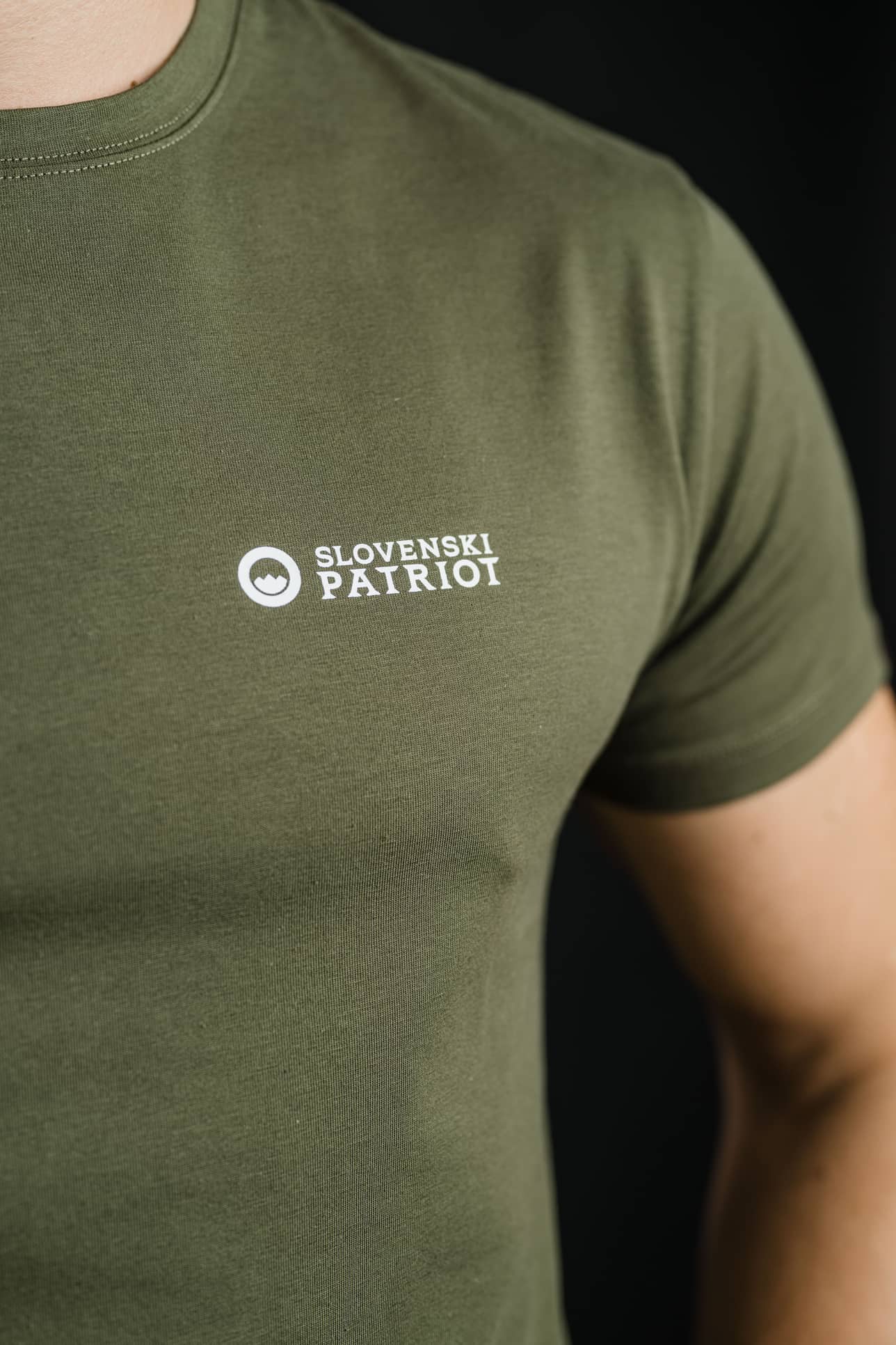 Bližnji posnetek logotipa Slovenski Patriot na olivno zeleni majici FIT, ki prikazuje natančen tisk in kakovostno tkanino, narejeno v Sloveniji.