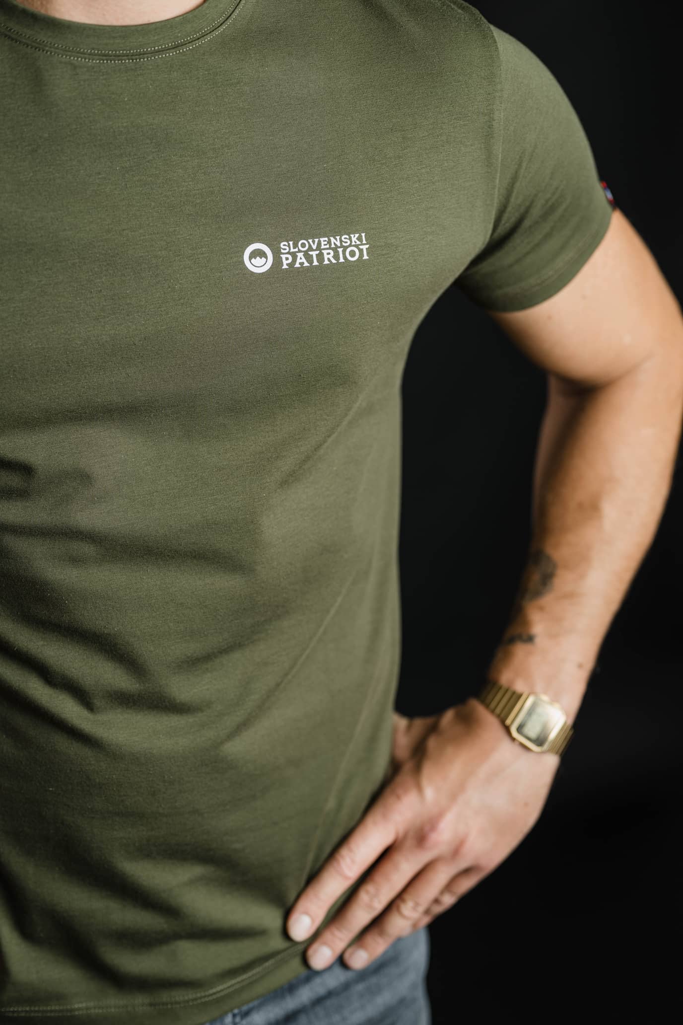 Detajl olivno zelene majice FIT znamke Slovenski Patriot, z belim logotipom na prsih, ki poudarja preprost, kakovosten in sodoben dizajn.
