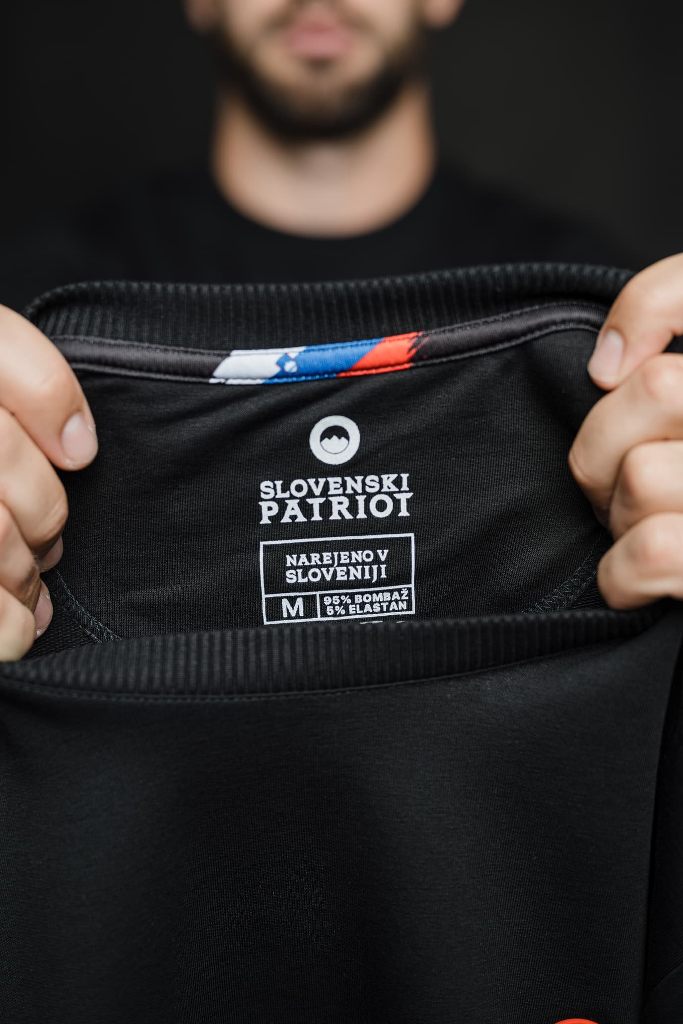 Notranja etiketa črnega puloverja Patriot Crew znamke Slovenski Patriot z napisom “Narejeno v Sloveniji”, narejenega iz 95 % bombaža in 5 % elastana, s potiskom slovenske zastave na notranji strani ovratnika.