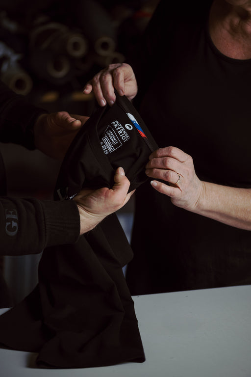 Dve osebi pregledujeta majico Slovenski Patriot z oznako “Narejeno v Sloveniji”. Prikaz lokalne, ročne izdelave oblačil.