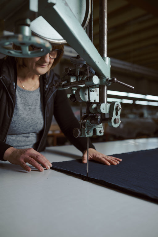 Šivilja reže blago s profesionalnim rezalnim strojem v slovenski proizvodnji. Prikaz natančnega in domačega obrtniškega dela.
